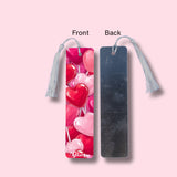 Two bookmark views, front side with a heart design and back side plain, on a pink background.
