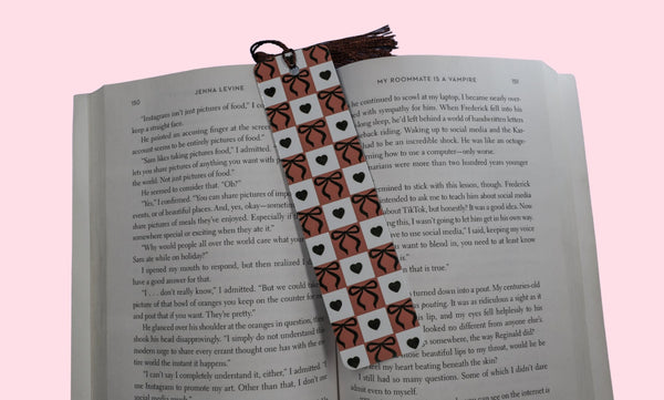 Book with a checkered bookmark with bows and hearts on a pink background