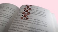 Open book with a magnetic bookmark with a checkered, black bows and black hearts design on a pink background 