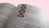 Open book with a magnetic bookmark with a checkered, black bows and black hearts design on a pink background 