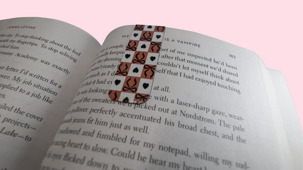 Open book with a magnetic bookmark with a checkered, black bows and black hearts design on a pink background 