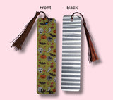front and back of a bookmark with tassels, one with a colorful halloween-themed pattern and the other an aluminum look on a pink background.