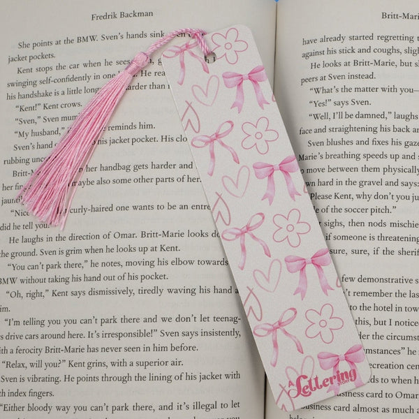 Pink aluminum bookmark with bows, hearts, and flowers on a book page