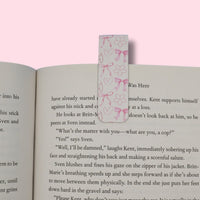 Open book with a pink bookmark featuring hearts and bows on a pink background