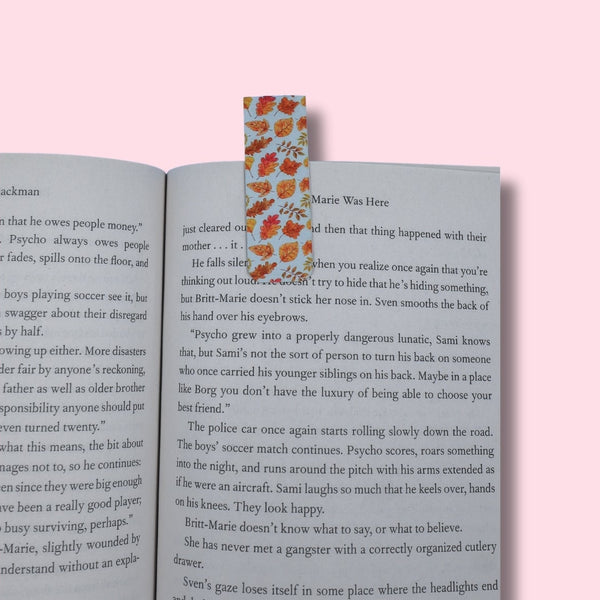 Open book with a bookmark featuring fall leaves on a pink background