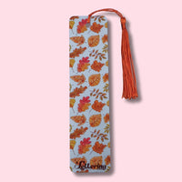 Bookmark with autumn leaf pattern and orange tassel on a pink background