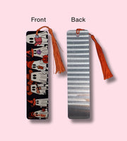 Front and Back side of a bookmark, one with a tassel on the front and another with an aluminum look design on the back, on a pink background.
