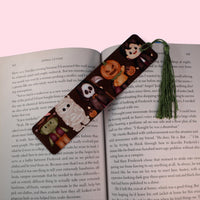 Decorative bookmark with cartoon characters dressed in halloween costumes on an open book against a pink background