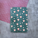 A tablet case with a dark green background patterned with pink and white hearts with #1 Mom quotes, shown from a top-down view on a textured gray surface with a pink patterned paper corner in the background.