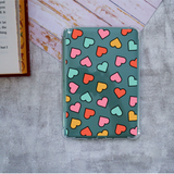 A clear protective reading tablet case with a teal background and a pattern of colorful hearts in pink, orange, yellow, and mint green, shown on a gray textured surface