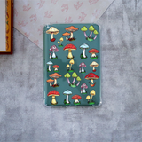 A clear protective Kindle case featuring a colorful printed design of various cartoonish mushrooms on a teal background, shown flat on a textured gray surface.