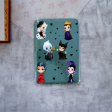 A clear protective case for a Kindle, featuring a printed design of six wittches on a teal background with small black hearts. The case is displayed on a textured gray surface.