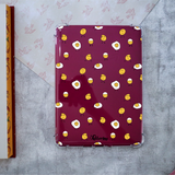 A clear protective Kindle case on a dark burgundy Kindle printed with a repeating pattern of cute cartoon fried eggs with smiling faces. The brand name 'A Lettering Story' is printed in black script near the bottom.
