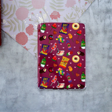 A hard-shell protective case for a Kindle, featuring a colorful cartoon candy and snack pattern on a Maroon background, displayed on a textured gray surface with a floral paper corner in the background.