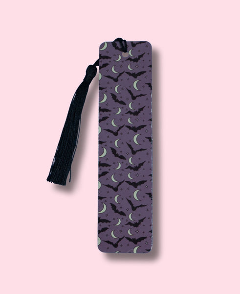 Purple bookmark featuring bats and crescent moons with a tassel on a pink background
