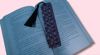Open book with a purple bookmark featuring bats and crescent moons on a pink background