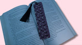 Open book with a purple bookmark featuring bats and crescent moons on a pink background