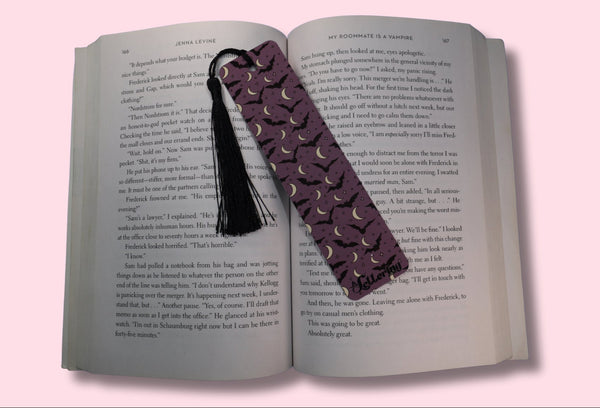 Open book with a purple bookmark featuring black bats and crescent moons on a pink background