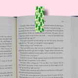 Book with a green pickles-themed bookmark on a pink background