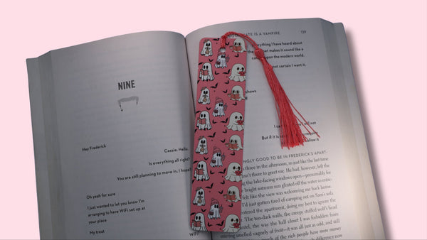 Open book with a pink bookmark featuring ghosts illustrations on a pink background
