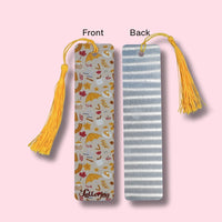 Front and Back side of bookmark, one with a fall theme pattern and yellow tassel, the other with an aluminum look and yellow tassel, on a pink background.