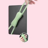A light green silicone wrist strap is shown attached to a black e-reader against a pale pink background. A hand is holding the strap, and a circular inset at the bottom shows a close-up of the strap worn on a wrist.
