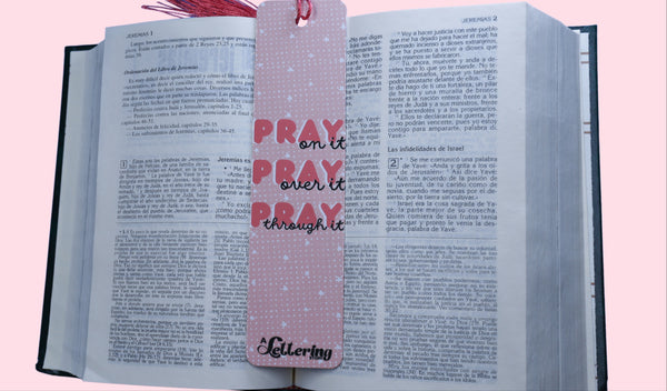 Open book with a pink bookmark featuring quote Pray on it, Pray over it, Pray through it on a pink background