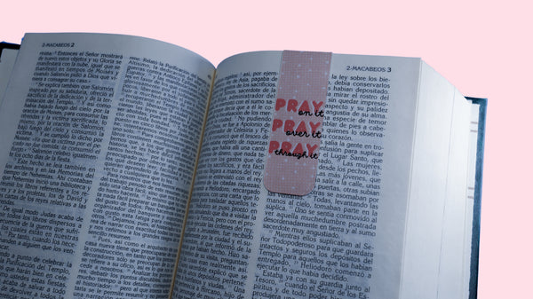 Open book with a pink bookmark with quote "Pray on it, Pray over it, Pray through it" on a pink background