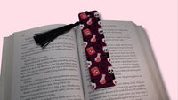 Book with a decorative bookmark featuring skulls, potion bottles, and spell books on a pink background