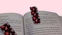 Two patterned magnetic bookmarks on an open book with a pink background
