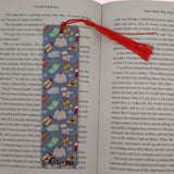 Open book with a cozy vibe bookmark featuring sweaters, fuzzy socks, hot chocolate and hats on a pink background
