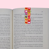 Open book with colorful heart-shaped bookmarks on a pink background